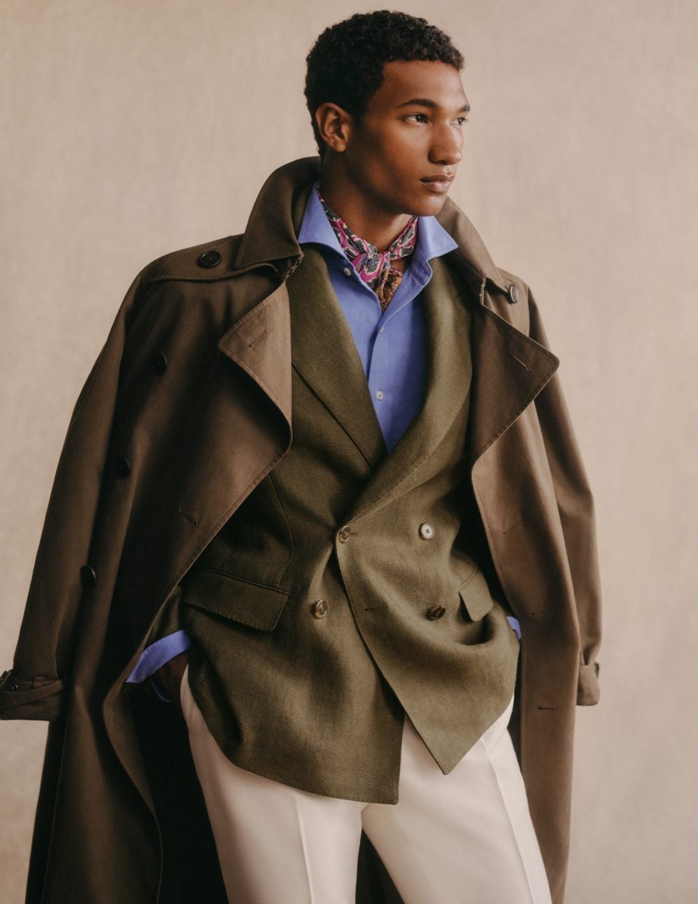 Man wears brown trench coat over double-breasted blazer and blue button-down.