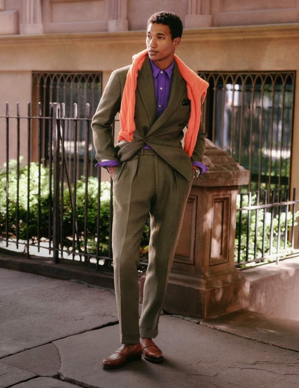 Man wears jacket over turtleneck sweater and white pleated pants.