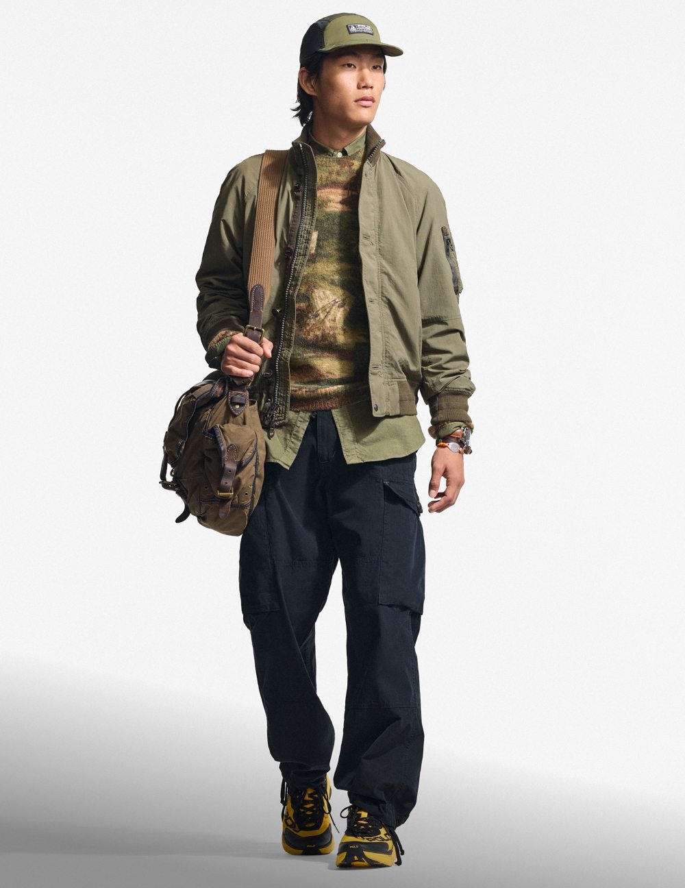 Man wears green jacket over print sweatshirt and navy cargo pants.