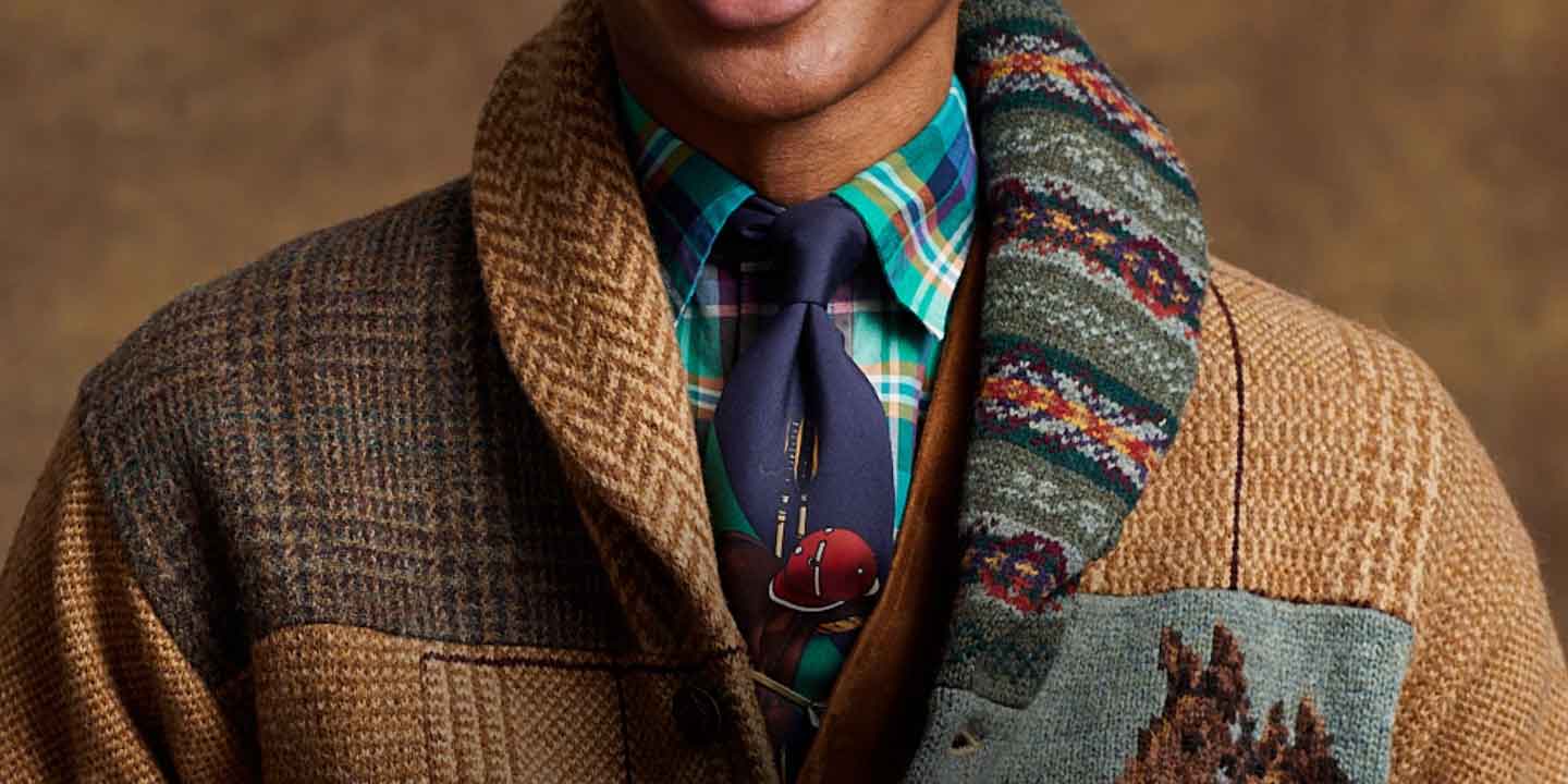 Man in patchwork tweed cardigan wears multicolored tie and plaid dress shirt.