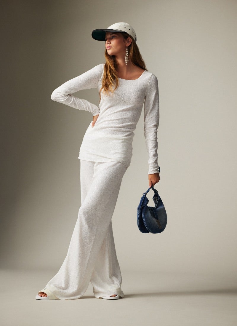 Woman wears oversize denim jacket over cream satin maxiskirt.