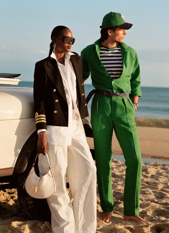 Woman and man on beach wear navy blazer over white outfit and green button-down and green trousers.