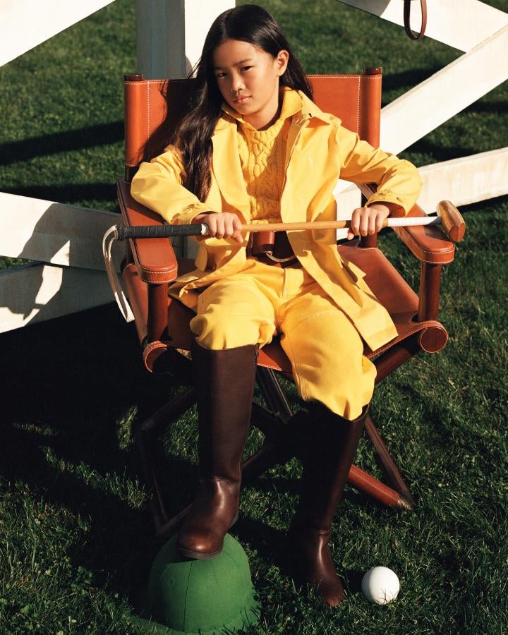 Girl in brown leather director’s chair wears yellow outfit and riding boots.